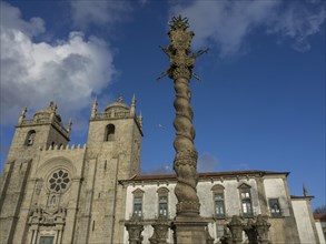 Gothic cathedral with a spiral column in the foreground under a clear blue sky, old houses in the