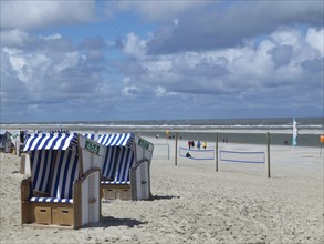 Blue and white beach chairs on the beach with people in the background in sunny weather, clouds on