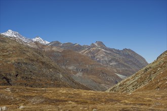 Vast valley between rocky mountains and mountain range under a bright blue sky, bare mountain peaks