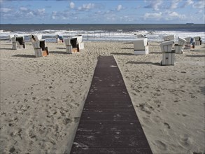 A wooden path leads to scattered white beach chairs on the sandy beach on a blue sky day with