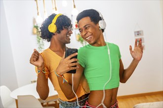 Gay latin male young couple dancing listening to music with headphones and mobile standing at home
