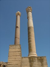 Two tall ancient columns in front of a clear blue sky, part of a ruined site, Tunis in Africa with