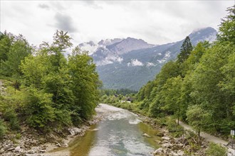 A river through a picturesque landscape with mountains and forests in the background under a cloudy