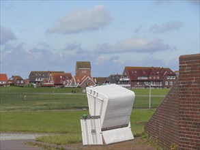 A single beach chair stands in a meadow in front of a row of typical North German houses under a