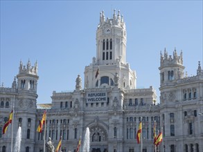 Magnificent white palace with towers, Spanish flags and a welcome banner for refugees, Madrid,