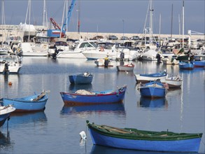 Several colourful boats lie quietly in the harbour water, The city of Bari on the Mediterranean