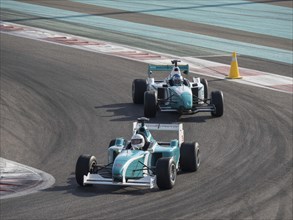 Two racing cars in a curve on the race track under a blue sky in a fast-paced competition, Abu