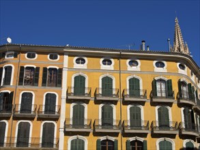 Yellow building with green shutters and numerous balconies in front of a clear blue sky, palma de