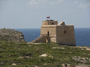 Historic tower with flag on the cliffs, surrounded by nature and the sea, the island of Gozo with