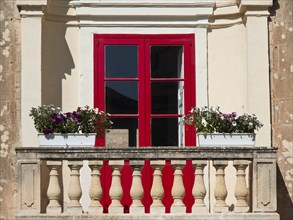 Red window with flower pots and historic stone balcony, old houses with balconies and towers, Gozo,