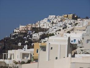 White houses spread out on a hill under a blue sky, The volcanic island of Santorini with blue and
