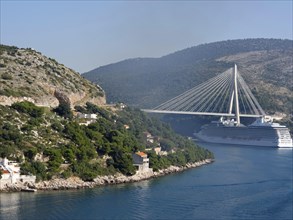 View of a coastline with green hills, a bridge and a cruise ship under a clear blue sky, the old