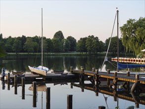 A sailing boat is moored at a jetty on the quiet lake, surrounded by green nature, green trees and