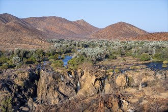 Kunene River with green vegetation in dry red mountain landscape, waterfall and African Baobab