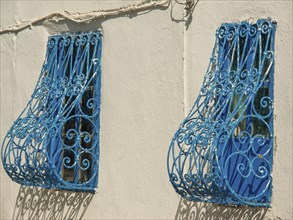 Two windows with decorative blue metal grilles on a light-coloured wall, Tunis in Africa with ruins