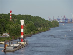Two red and white striped lighthouses on a river bank, in the background harbour facilities and