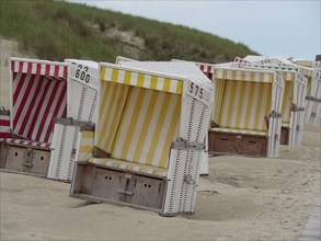 Colourful beach chairs in a row on the sandy beach, surrounded by dunes, pleasant weather without