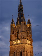 Illuminated clock tower with gothic elements in the evening, blue hour in a medieval town with