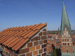 Brick roof and church tower dominate the view of a medieval town with clear blue sky, red brick