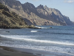 Coast with sandy beach, waves and imposing rocky mountains in the background, tenerife, spain