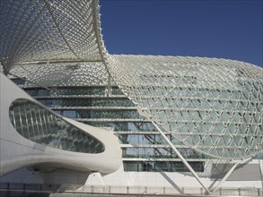 Modern building with a striking grid structure and many glass surfaces under a bright blue sky, Abu