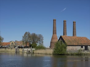 Historic buildings with three tall chimneys and a small water channel under a clear sky, Enkhuizen,