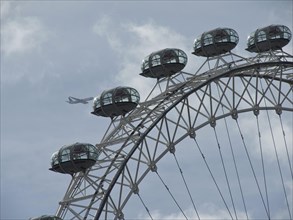 Detail of the Ferris wheel with a view of the capsules and an aeroplane flying past in the sky,