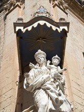 Expressive Madonna statue with child under an elaborate stone canopy on a historic facade, the town