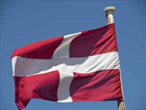 Danish flag flies on a flagpole against a clear sky, the town of mdina on the island of malta with