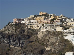 A hill dotted with whitewashed houses rises against a clear blue sky in Santorini, The volcanic