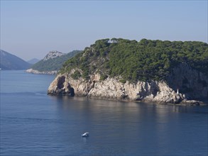 Forested island with steep cliffs on the calm blue sea, the old town of Dubrovnik with historic