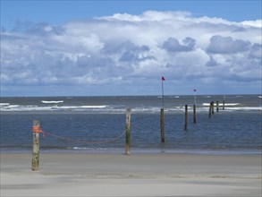 Sandy beach beach with poles and red flags in the water, cloudy sky, view of the wide sea with
