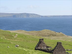 Ruins of an old building on green hills overlooking the blue sea and distant cliffs under a clear