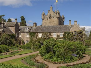 Medieval castle with towers and well-kept garden area under a blue sky, old grey stone building in