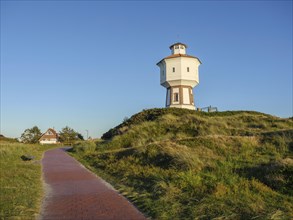 Lighthouse on a hill on a cobbled path with green landscape and houses in the background under a