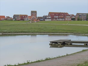 Pond with a wooden jetty and a village with red roofs in the background, Baltrum Germany