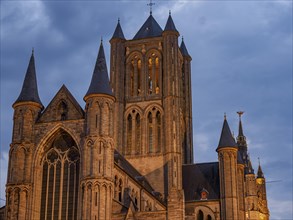 A gothic church with striking towers and illuminated windows at dusk against a cloudy sky, historic