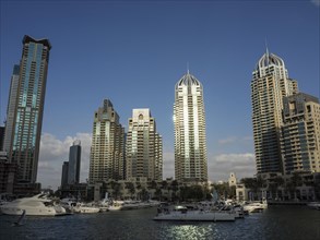 Boats in a marina in front of a row of modern skyscrapers under a cloudless sky, Dubai, Arab