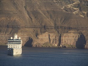 Another cruise ship sails along the sea, again with steep cliffs in the background, The volcanic