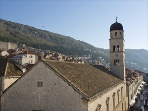 A bell tower rises above a church in a medieval town that stretches along a sunlit hill, the old