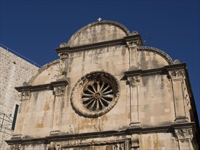 An old church with a detailed stone facade and a rose window under a clear blue sky, the old town
