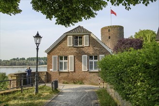 A house and a castle tower made of bricks with path, lantern and river in the background, rhine