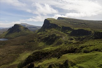Quiraing, landscape in Scotland, view of rugged mountains and wide plains under a half-cloudy sky