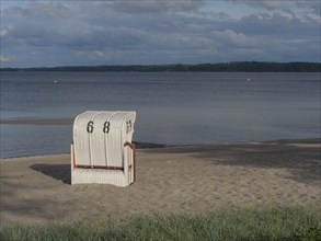 Single white beach chair on deserted sandy beach, with cloudy sky and calm sea, colourful beach