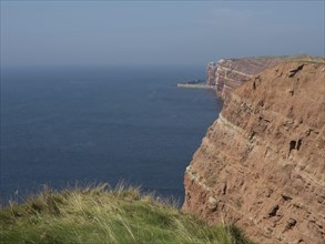 A vast coastal landscape with red cliffs and deep blue sea under a clear sky, Heligoland, Germany,