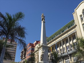 Monumental statue between palm trees and historic buildings under a blue sky, Tenerife, Spain,
