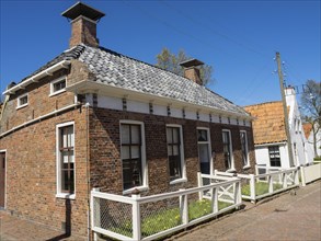 Brick house with white fence on a rural road under a clear blue sky, Enkhuizen, Nirderlande