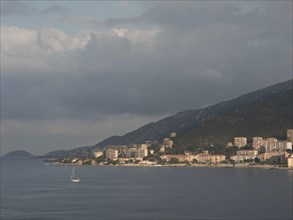 Urban coastal view with buildings on a hill, dark clouds and calm sea, Corsica, ajaccio, France,