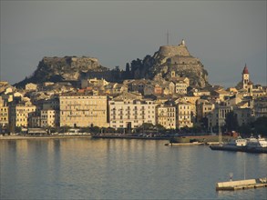 Historic town with a large fortress on a hill, surrounded by numerous buildings and a quiet harbour