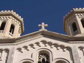 Close-up of the church facade with two towers and a cross under a deep blue sky, the old town of